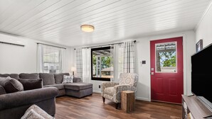 A modern living room with a sectional sofa, a patterned armchair, and a wooden coffee table. - Pleasure Point Place WATERFRONT Cottage (Florien)