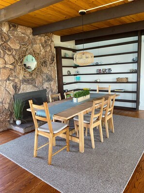 A dining area with a stone wall, wooden ceiling, and a fireplace. - Oceanfront Oasis, Sunsets & Crashing Waves (Moss Beach)