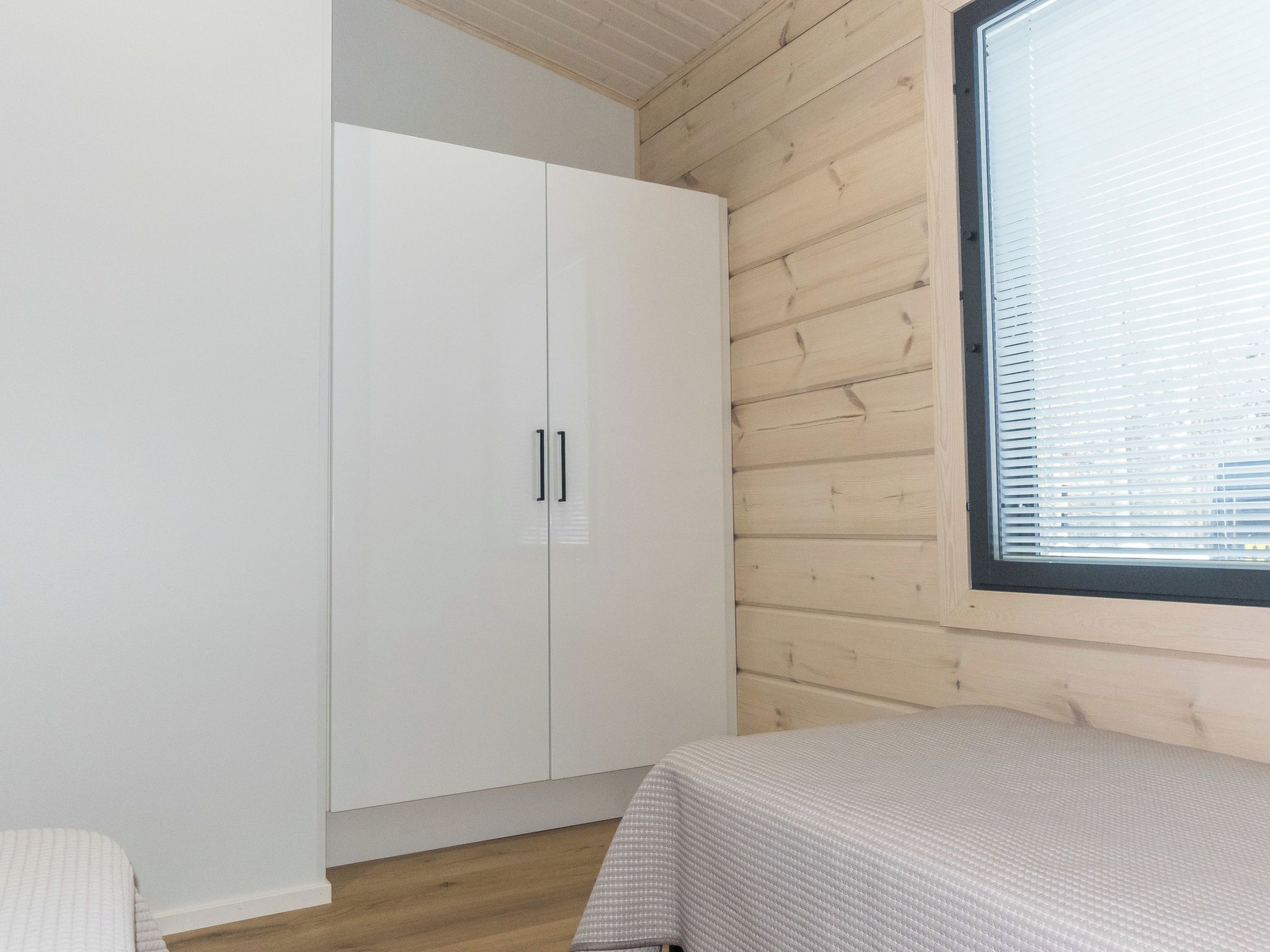 Een slaapkamer met een houten plafond, een witte kledingkast, een raam met zonwering en een bed met een witte hoes.