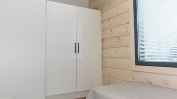 Een slaapkamer met een houten plafond, een witte kledingkast, een raam met zonwering en een bed met een witte hoes.