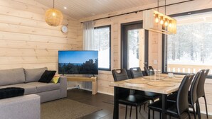 Een moderne woonkamer met een bank, televisie, eettafel, stoelen en grote ramen.