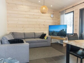 A modern living room with a grey sofa, a flat-screen TV, and a wooden ceiling.