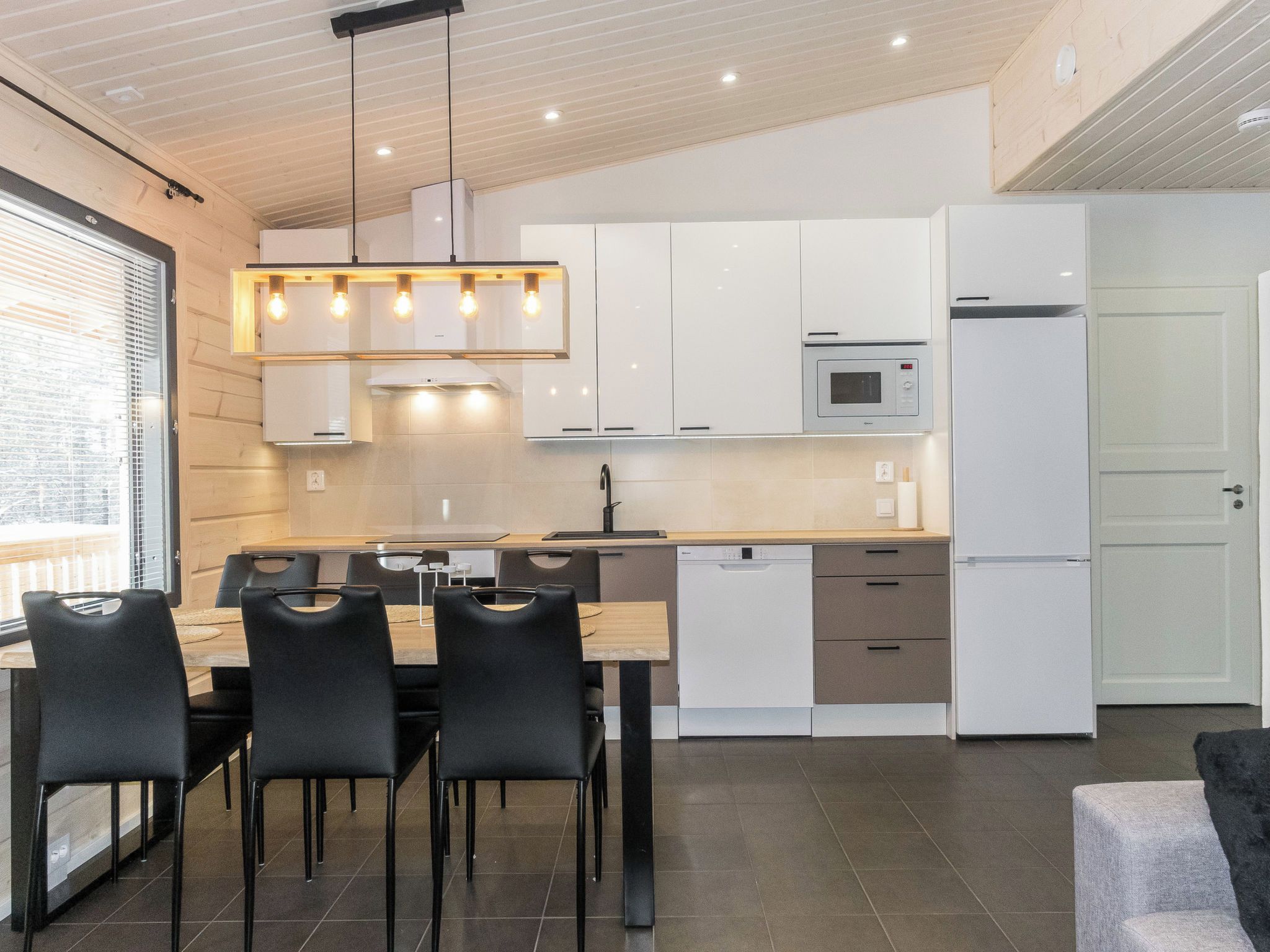 Een moderne keuken met witte kasten, een ingebouwde magnetron en een eethoek met een houten tafel en zwarte stoelen.