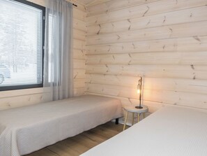 Ein Zimmer mit zwei Einzelbetten, einem Fenster mit Jalousien und einem kleinen Tisch mit Lampe.