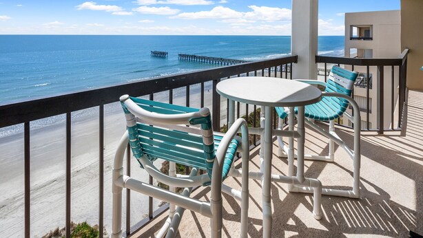 Ein Balkon mit Blick auf das Meer und einen Steg, ausgestattet mit zwei Stühlen und einem kleinen Tisch.