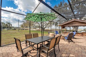 A covered patio with a table and chairs, a grill area, and a view of a lake and trees.
