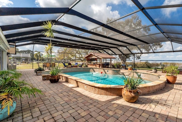 A covered outdoor swimming pool with a patio area, lounge chairs, and a bar.