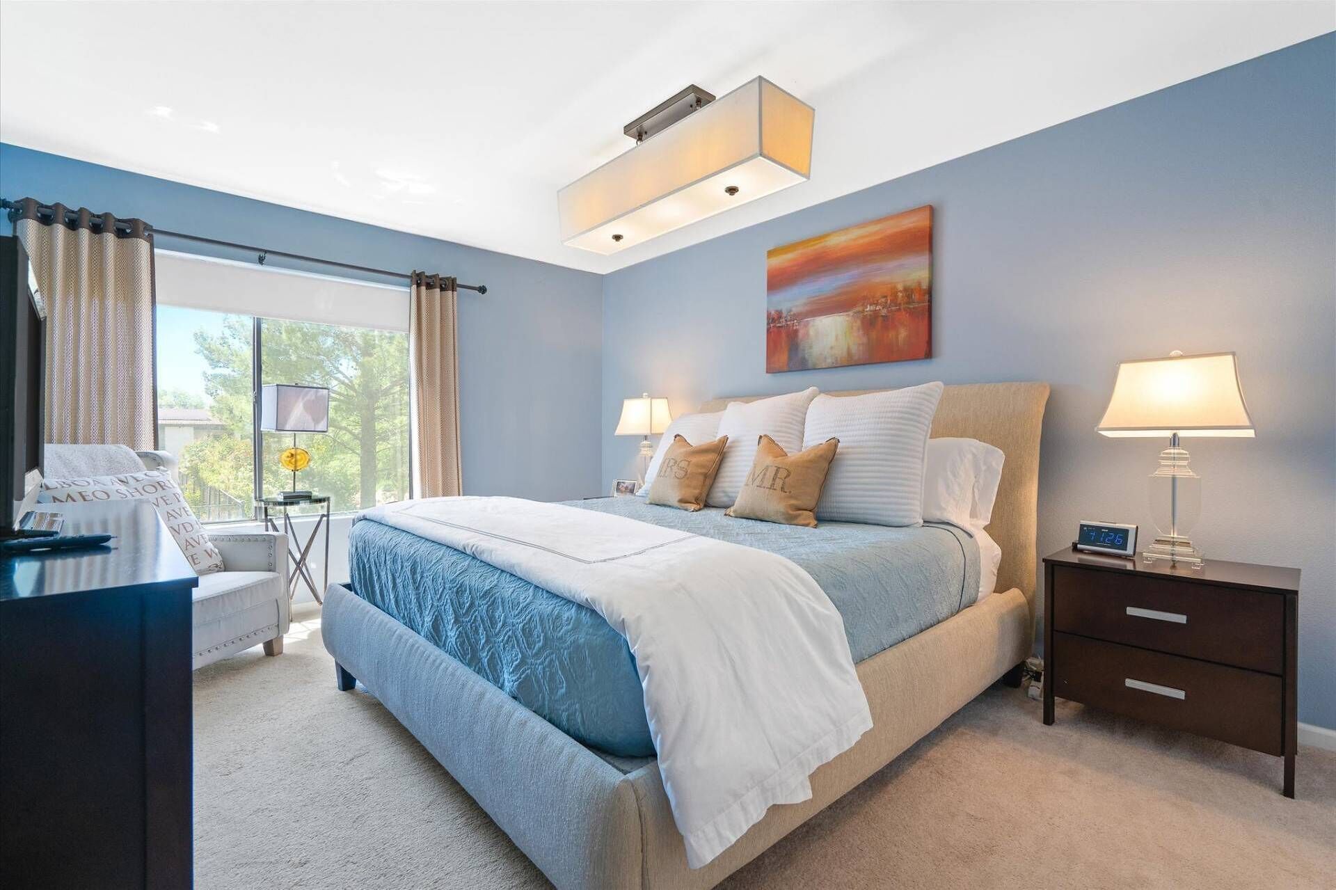 A bedroom with a bed, bedside tables, a desk, and a window with curtains.