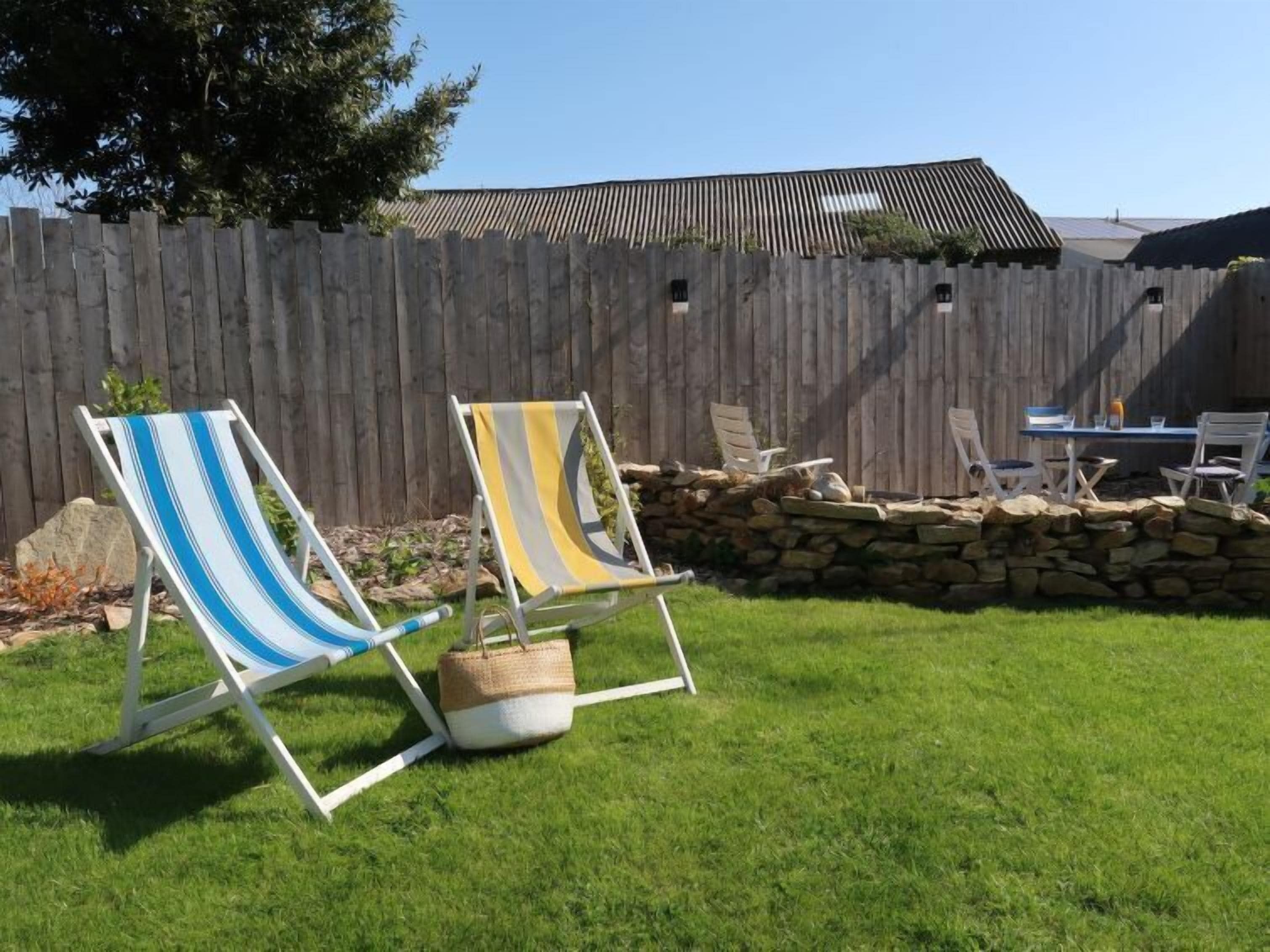 A backyard with two striped lawn chairs, a stone wall, and a wooden fence.