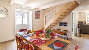 A dining area with a wooden table set for four, red chairs, and a staircase leading to another room.