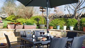 Une terrasse extérieure avec une table et des chaises, entourée de plantes en pot et d’un mur de pierre.