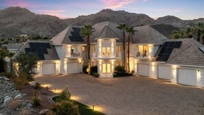 A multi-story house with solar panels, a driveway, and a mountainous backdrop. - The Desert Castle with a Movie Theatre, golf, game room, sleeps 23 (Palm Desert)