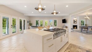 A spacious kitchen with a large island, modern pendant lights, and a fireplace. - The Desert Castle with a Movie Theatre, golf, game room, sleeps 23 (Palm Desert)