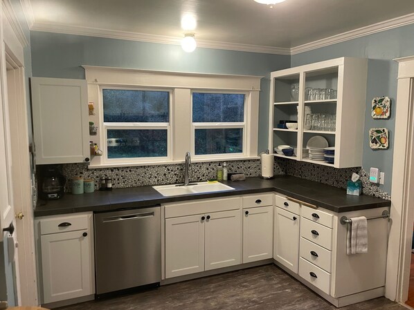 A kitchen with white cabinets, a black countertop, a window with a view, and a tiled backsplash. - Stunning views, 6-Bedroom Farmhouse with beach access and mooring (Eastsound)