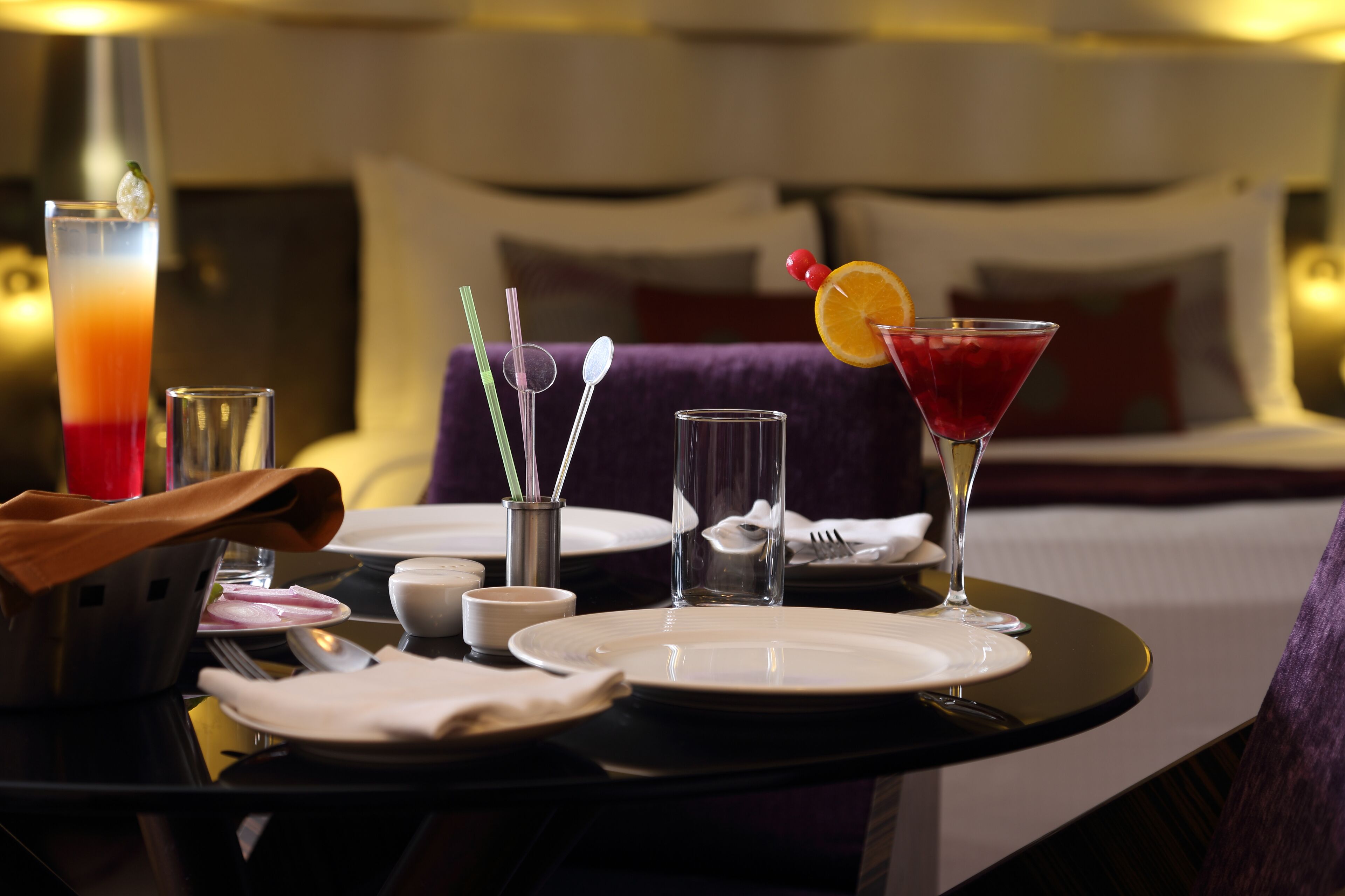 A hotel dining table set with plates, glasses, and a martini glass with an orange garnish.