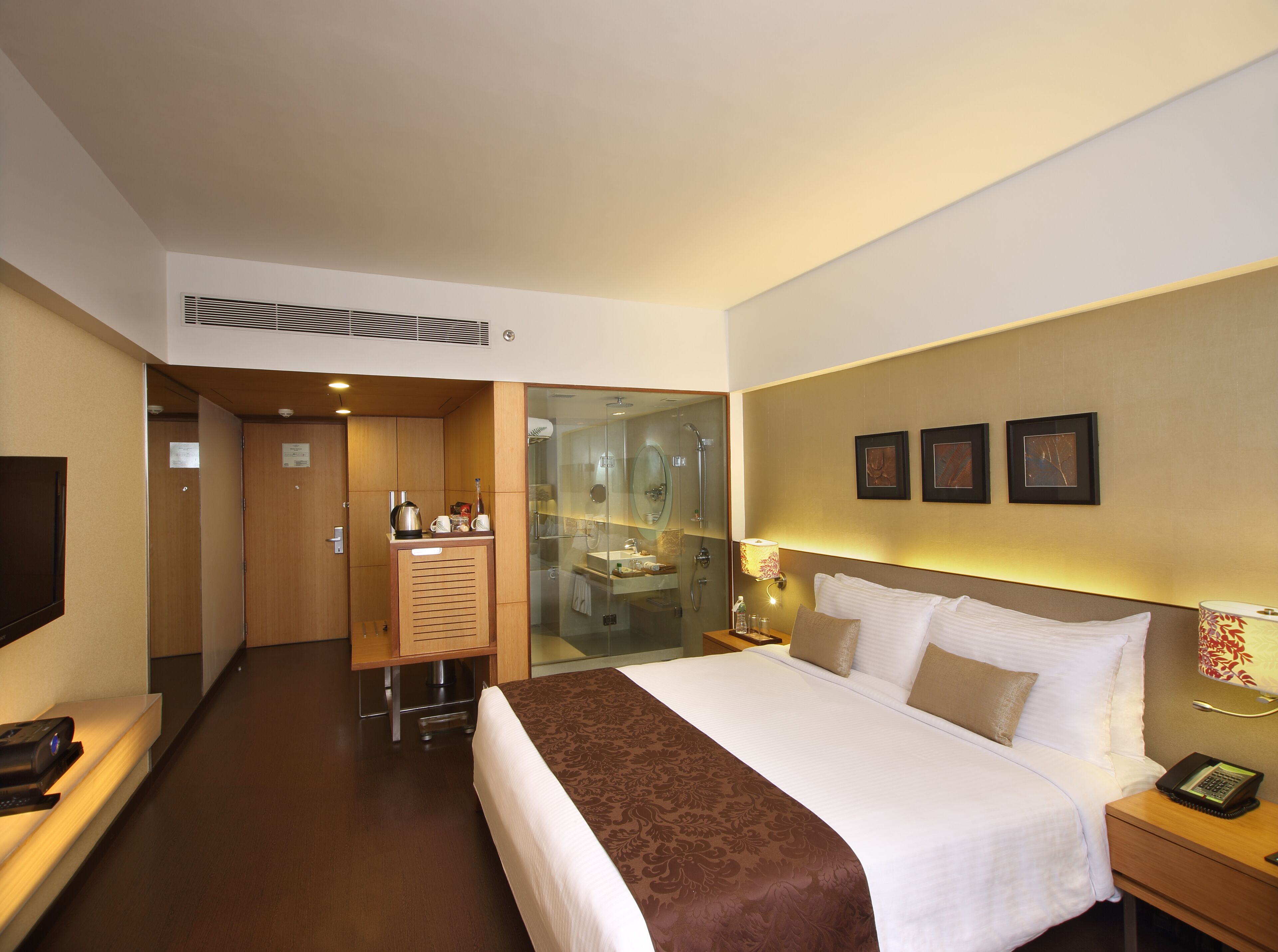 Habitación de hotel con una cama grande, un escritorio con teléfono, un espejo y un baño visible a través de una puerta de cristal.