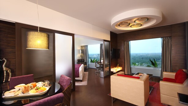 Una habitación de hotel moderna con comedor, zona de estar con sofá y sillón, cama y un ventanal con vistas.
