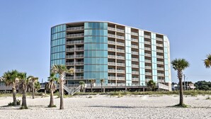 Ein mehrstöckiges Hotel mit bogenförmiger Fassade, gelegen an einem Sandstrand mit Palmen.