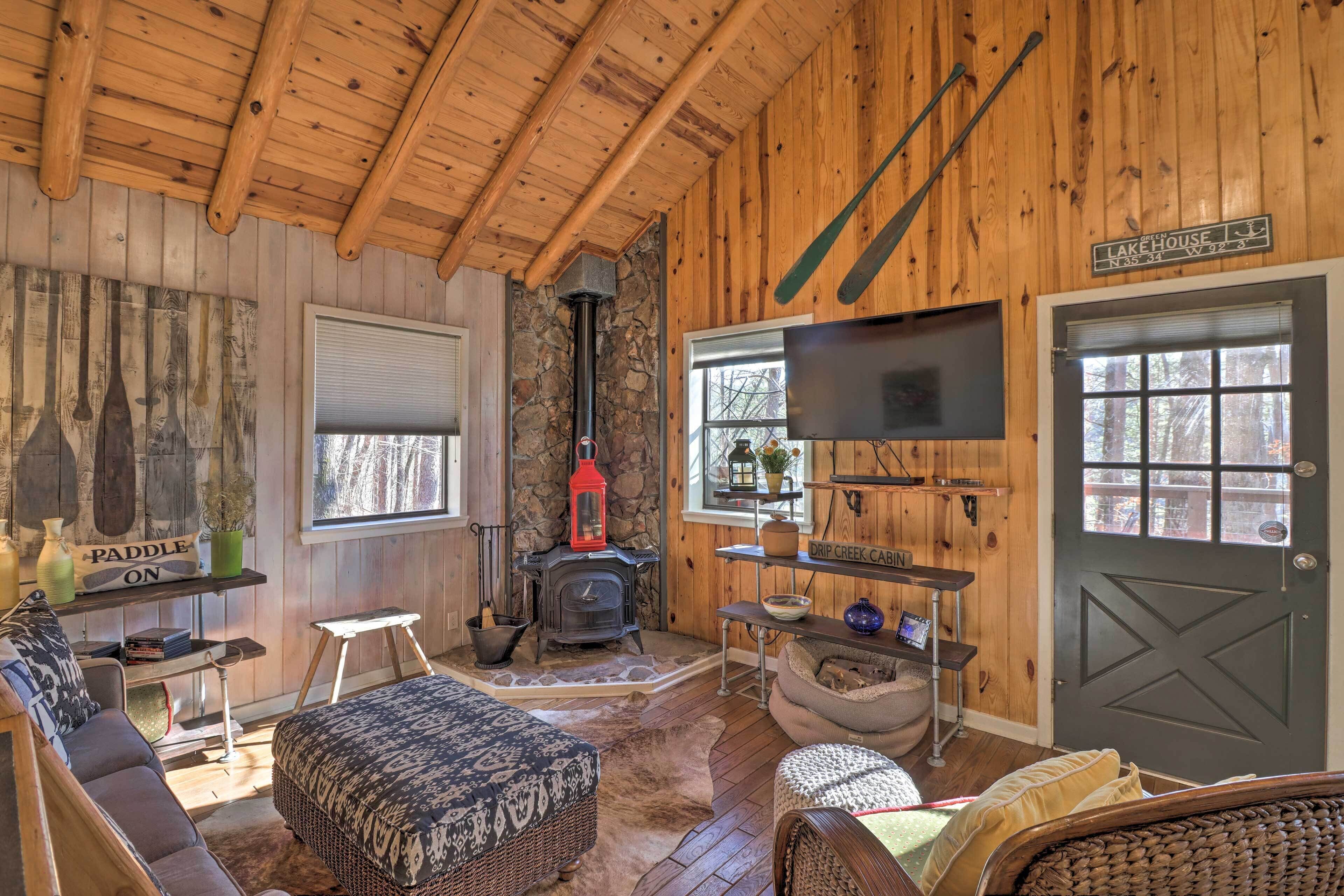 A cozy cabin interior with a stone fireplace, a television mounted on the wall, and a sign indicating the name 'Lake House'.