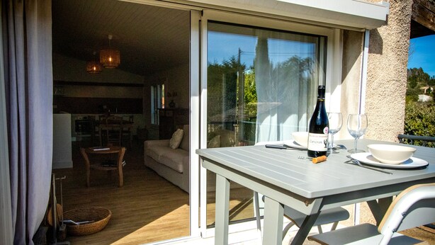 A dining area with a table, chairs, a bottle of wine, and glasses. - Gîte for two with private pool 20 minutes from Narbonne (Montséret)