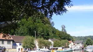 A calm river with boats docked along the shore, surrounded by residential buildings and lush greenery. - Wintersbourg Spa Retreat (Wintersbourg)