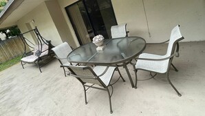 Eine Terrasse mit einem Glastisch und vier Stühlen, einem Hängesessel und einer dekorativen Schale auf dem Tisch.