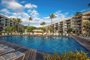 A hotel with a swimming pool, palm trees, and a clear sky.