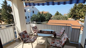 En balkon med et bord og stole, udsigt til kvarteret og et tegltag i baggrunden.