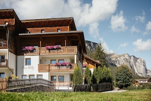 A multi-story wooden building with balconies, a stone wall, and a mountain backdrop.