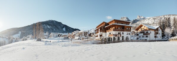 Un complejo turístico en la montaña cubierto de nieve, con edificios de madera, pistas de esquí y un cielo despejado.