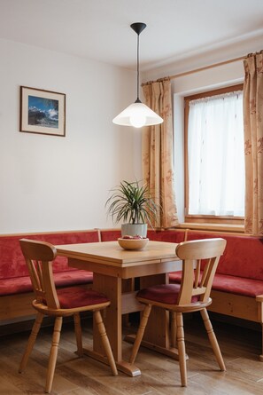 Un comedor con una mesa de madera, dos sillas, una planta en maceta, una lámpara colgante, un banco acolchado y un cuadro en la pared.