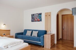 Un dormitorio con una cama, un sofá azul, un aparador de madera, un cuadro y una puerta de madera.