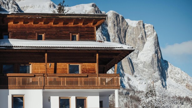 Una cabaña de madera con balcón, con montañas nevadas al fondo.