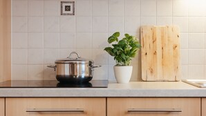 Una cocina con estufa, olla, planta en maceta y tabla de cortar de madera.
