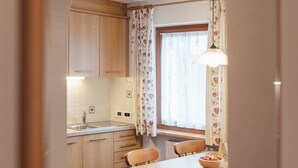 Una cocina con armarios de madera, una mesa de comedor con sillas, una ventana con cortinas y una lámpara colgante.
