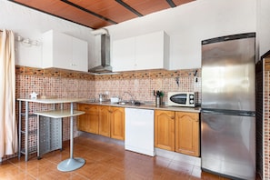 A kitchen with a microwave, refrigerator, wooden cabinets, and a tiled backsplash.