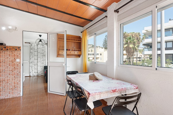 A compact kitchen with a dining area, a wooden ceiling, and a view of buildings through large windows.