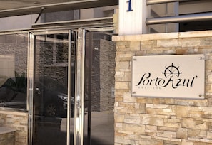 Une porte d’entrée en verre, un mur de pierre et une enseigne portant l’inscription « Portofzul Edificio » ainsi que le logo d’une roue de navire.