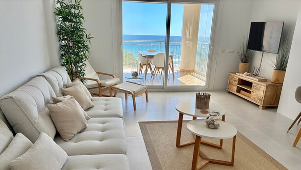 Ein modernes Wohnzimmer mit einer Couch, Sesseln, einem Couchtisch, einem Fernseher und Meerblick.