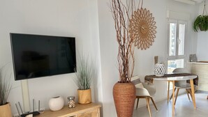Ein modernes Wohnzimmer mit Flachbildfernseher, einer Holzunterhaltungsecke, Esstisch, Stühlen und Zimmerpflanzen.