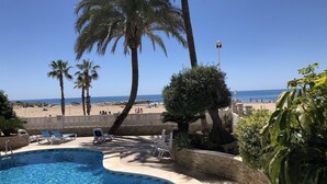 Ein Pool mit Liegestühlen, Palmen und Blick auf den Strand.
