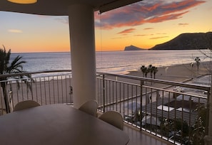 Un balcón con vista al océano al atardecer, una mesa y sillas.