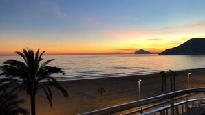 Ein Strand mit Sonnenuntergang, Palmen und einem fernen Berg.