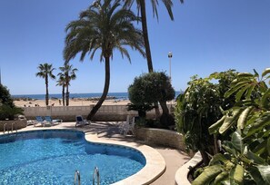 Una piscina con sillas de descanso, palmeras y vistas a la playa.