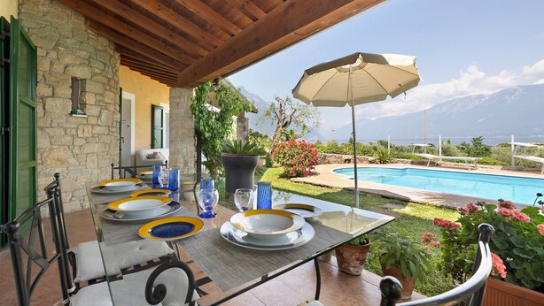 A covered outdoor dining area with a pool view, stone walls, and potted plants. - Villa Corneghe with Lake View, Pool, Garden, and Terrace (Gargnano)
