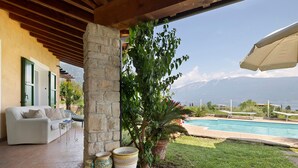 A covered patio with a pool, a white sofa, and a view of mountains. - Villa Corneghe with Lake View, Pool, Garden, and Terrace (Gargnano)
