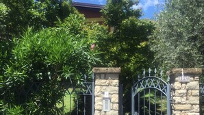 A gated entrance with stone pillars and metal gates, surrounded by lush greenery and a clear blue sky. - Villa Corneghe with Lake View, Pool, Garden, and Terrace (Gargnano)
