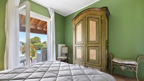 A bedroom with a large bed, a wardrobe, a chair, and a view of the outdoors. - Villa Corneghe with Lake View, Pool, Garden, and Terrace (Gargnano)