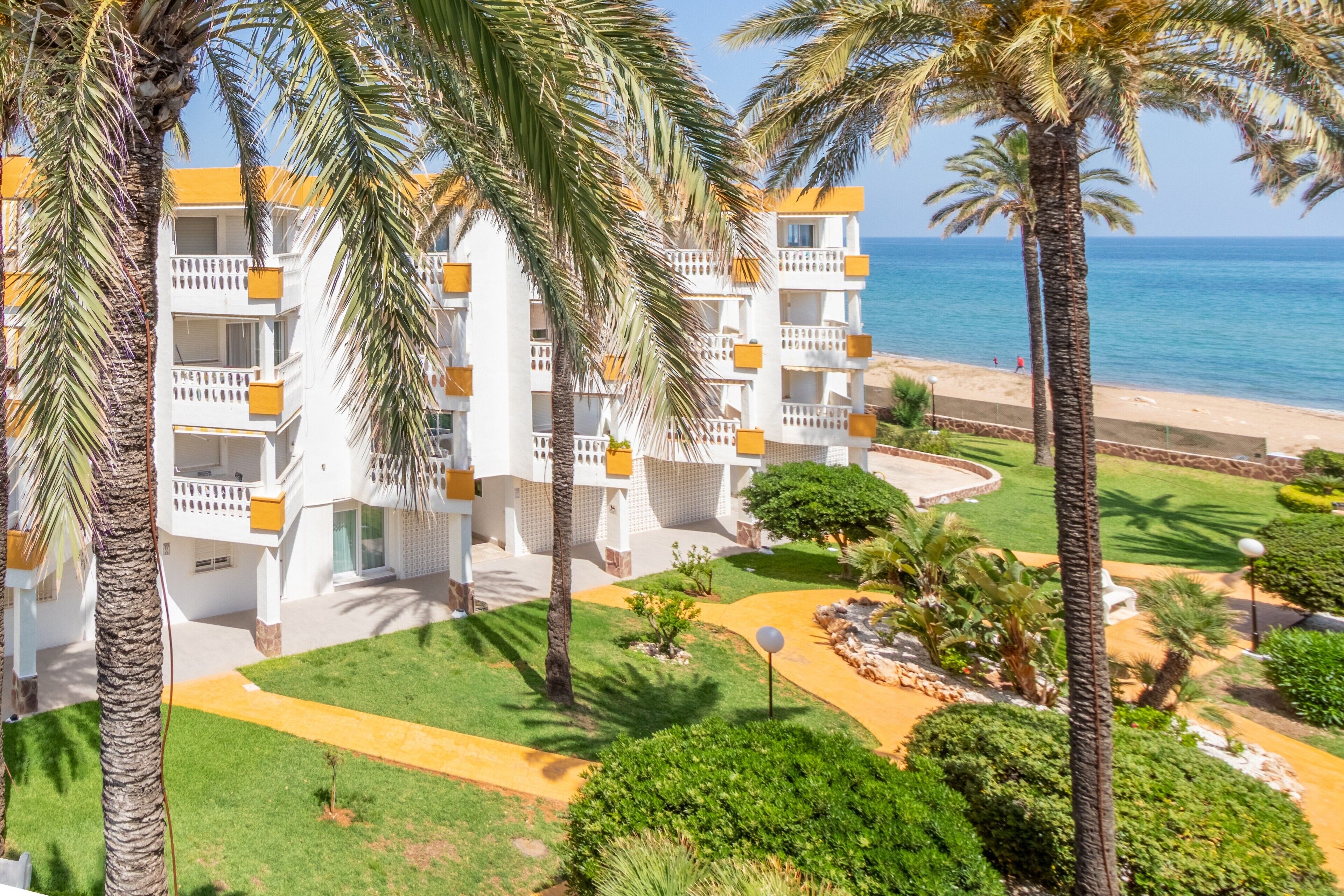 Un hotel con varios pisos, balcones y un jardín bien cuidado con palmeras y senderos.
