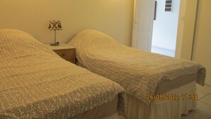 A room with two beds, a nightstand with a lamp, and a door leading to another room. - Appartement en sous-sol.Jardin privé. Situé dans un village des montagnes noires (Labastide-Rouairoux)